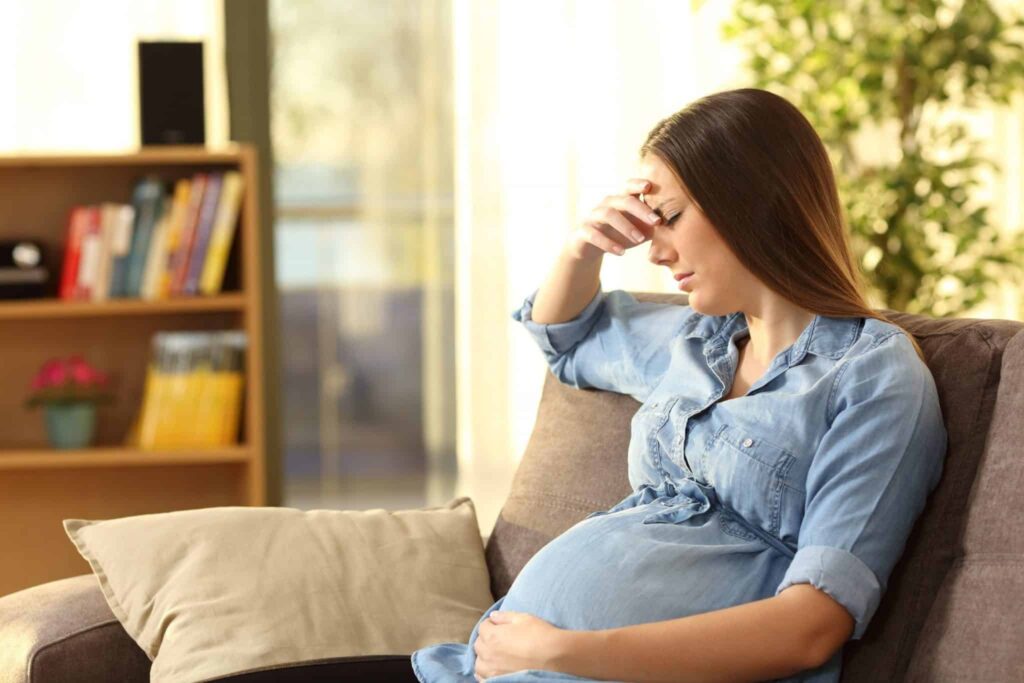 Worried pregnant woman at home on her couch.